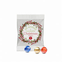 Drei LINDOR-Pralinés vor einem individuell bedruckten Papierbeutel mit Weihnachtsmotiv