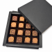 Schwarze Sechzehner-Pralinébox mit goldverzierten Pralinés und geöffnetem Deckel